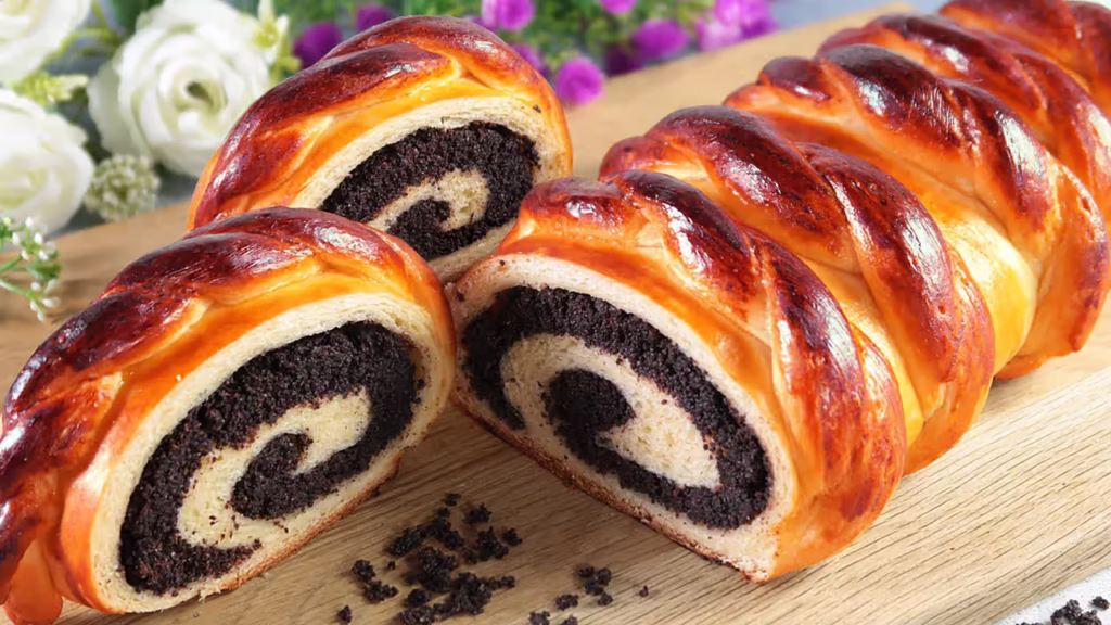 A sliced braided poppy seed roll on a wooden cutting board.